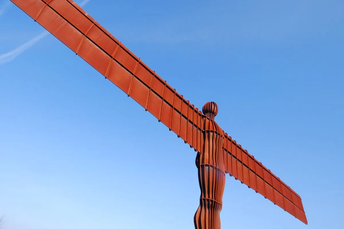 De Angel of the North van opzij, zodat de dunne vleugels en het massieve lijf allebei te zien zijn, met de heuvel eronder.