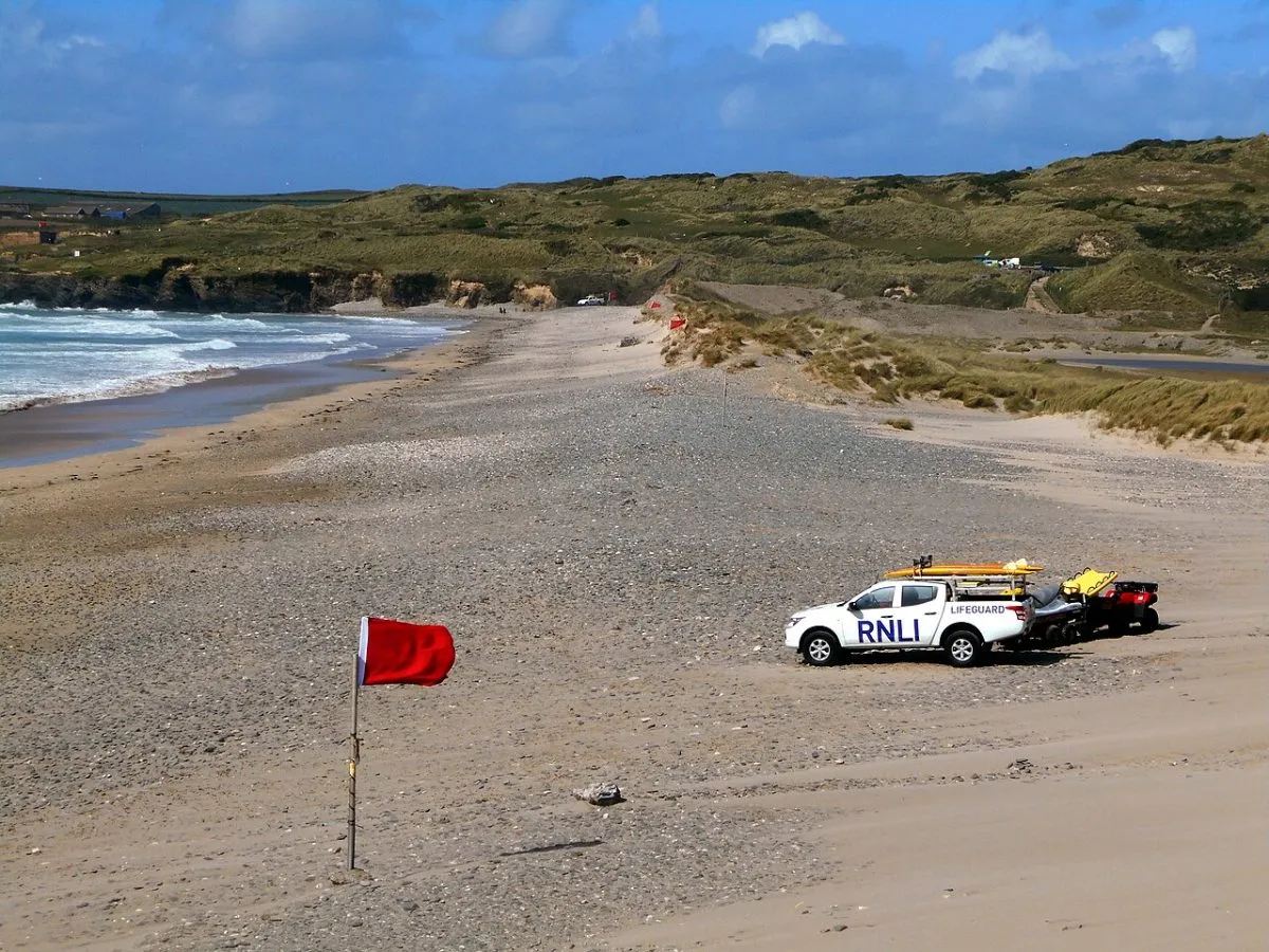 Het strand van Mawgan Porth met de vlaggen van de RNLI in beeld, of Porthcothan bij laag water.
