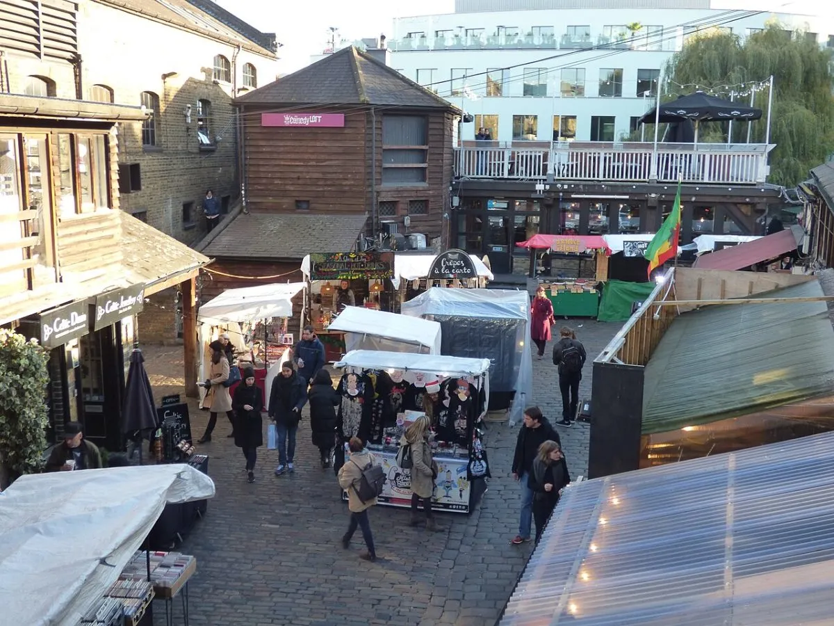 Een foodcourt in vol bedrijf: kramen naast elkaar met bordjes en mensen die staan te eten. Liefst het overdekte deel bij Camden Lock of Hawley Wharf.