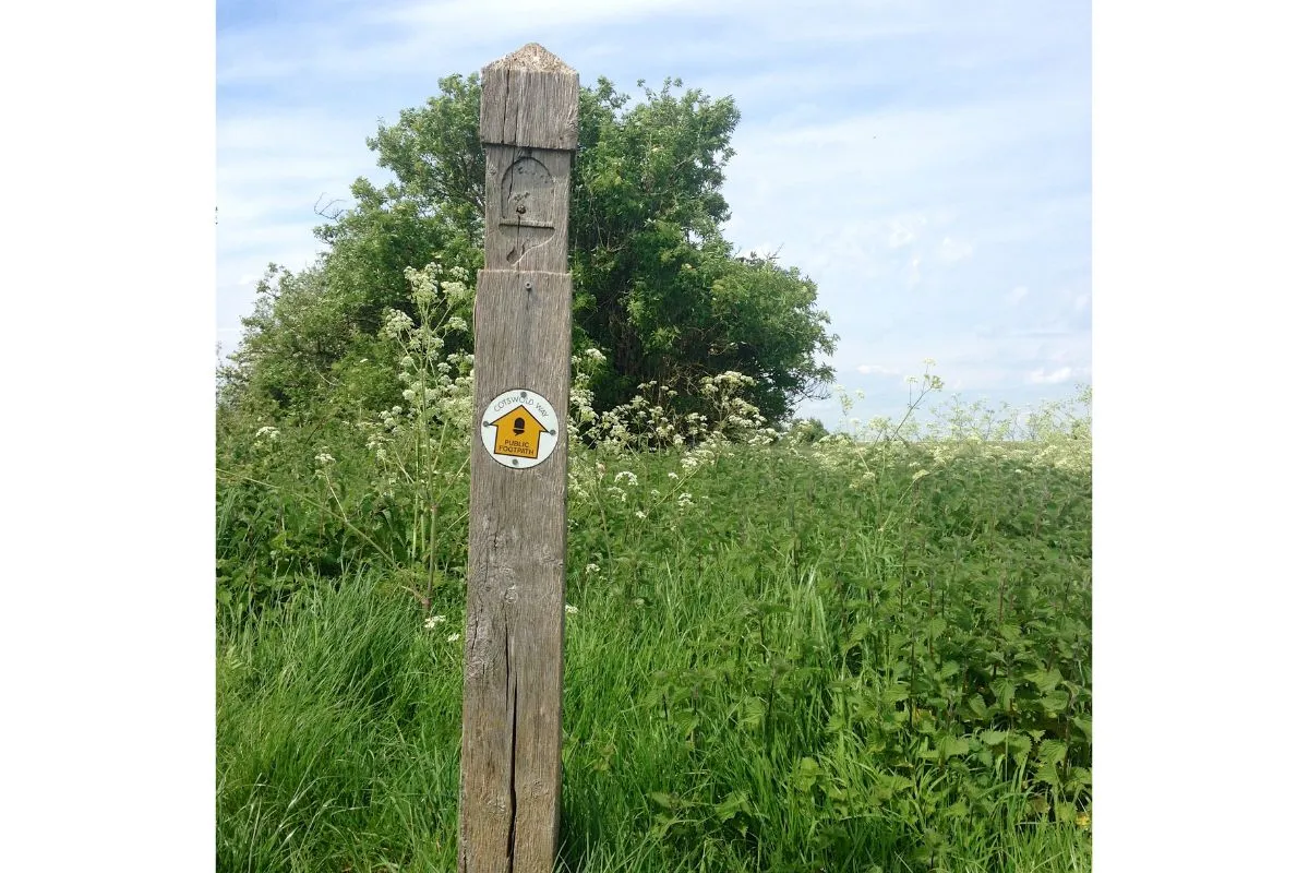 Een wegwijzer of paal langs het pad met het eikeltje van de National Trails en de naam Cotswold Way, met het pad erachter.