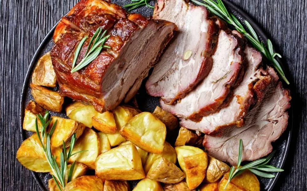 Een Sunday roast op tafel: vlees, geroosterde aardappelen, groente, een Yorkshire pudding en jus. Van bovenaf of schuin, zodat alle onderdelen zichtbaar zijn.