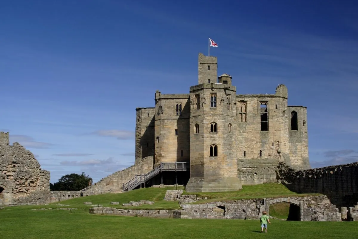 Warkworth Castle vanaf de brug of vanaf de rivier de Coquet, met het dorp ertussen. De kruisvormige donjon mag herkenbaar zijn.