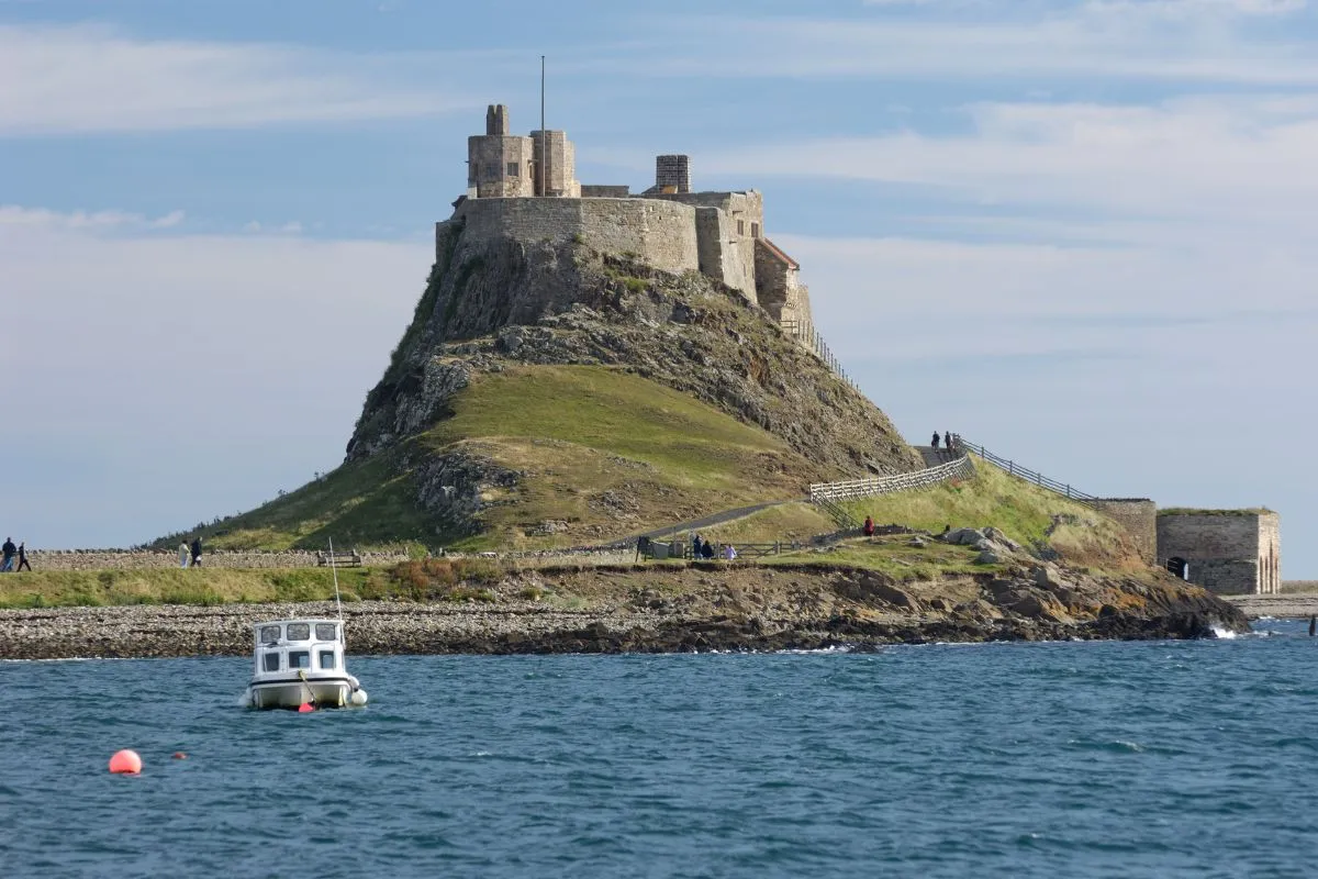 Lindisfarne Castle op zijn rotsplateau, gezien vanaf de haven, met de omgekeerde vissersboten op de voorgrond. Dat is het beeld waar het eiland om bekend staat.