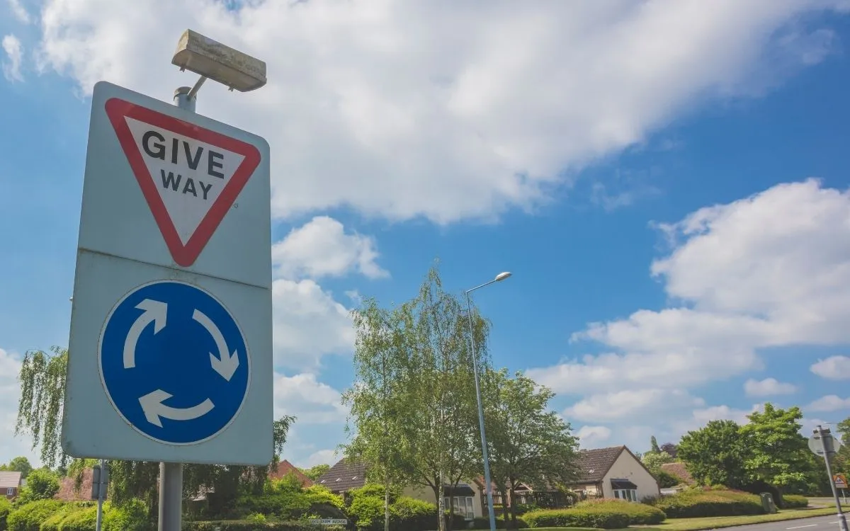 Een Engelse mini-rotonde van ooghoogte of vanuit de auto: het witte geschilderde rondje op het wegdek, met de pijlen eromheen. Juist geen grote rotonde.