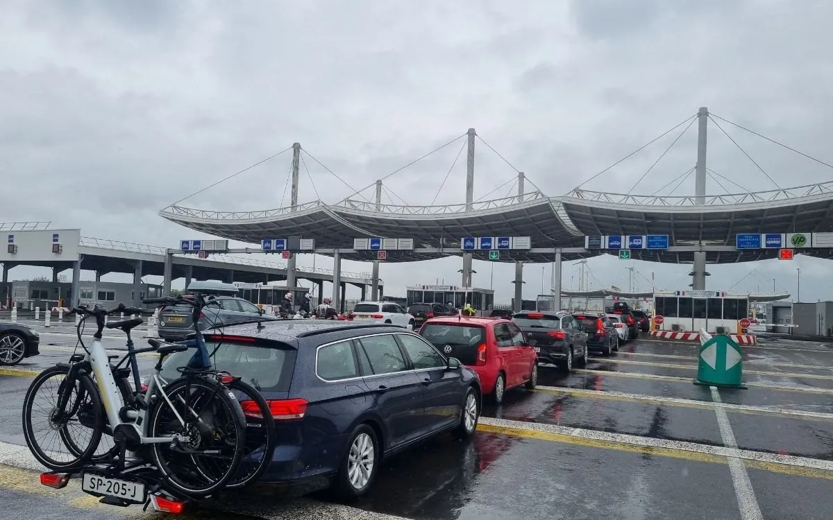 De ingang van de UK Terminal in Amsterdam Centraal, met de bewegwijzering en reizigers met koffers ervoor.