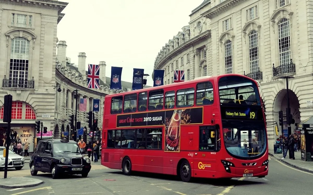 Een rode dubbeldekker bij een halte in Londen, met de kaartlezer bij de deur zichtbaar.