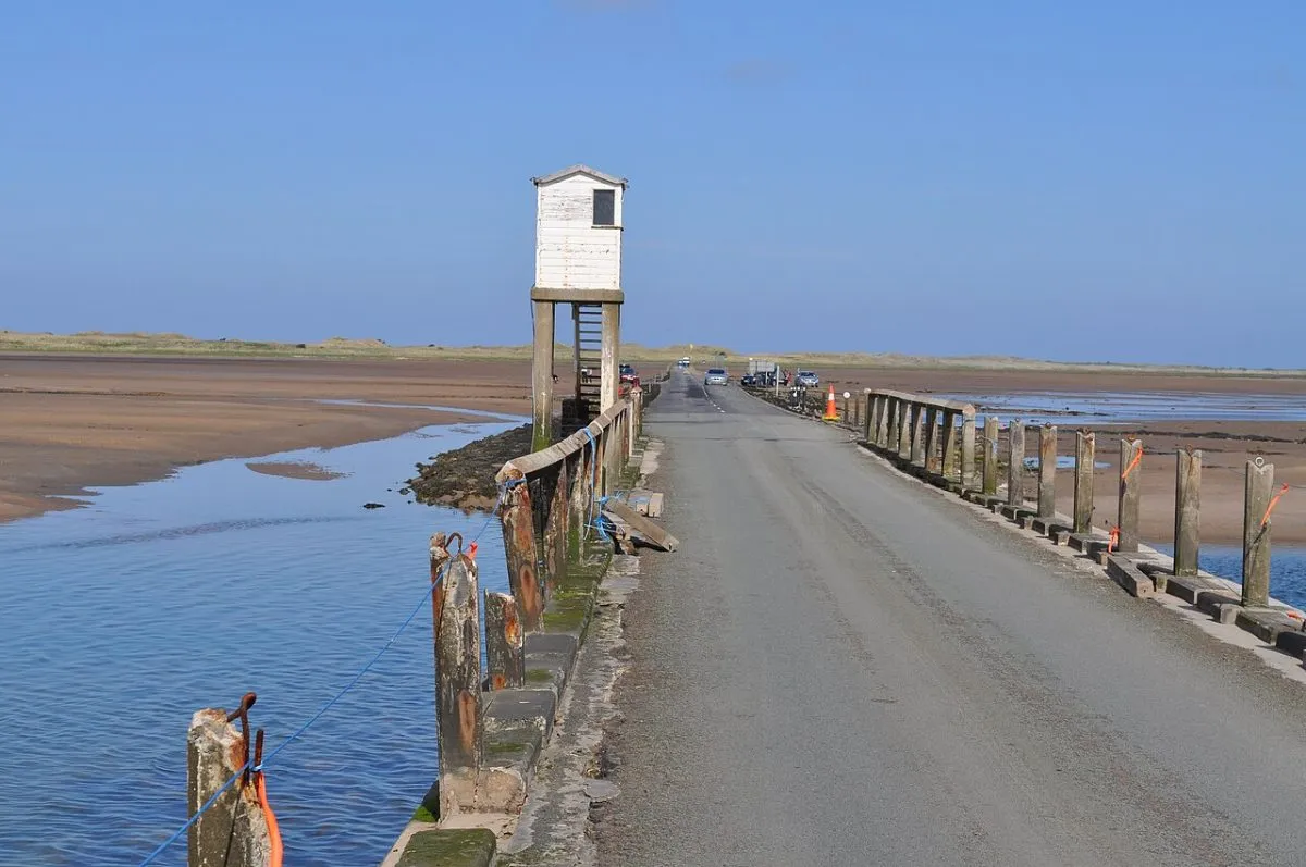De causeway naar Holy Island bij laag water, met de weg die het wad in loopt en de palen of de vluchthut erlangs.