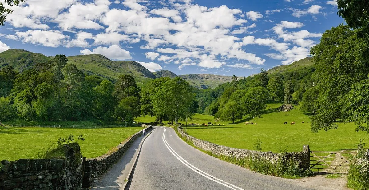 Een weg door het Lake District tussen de heuvels, met een meer of een pas in beeld.