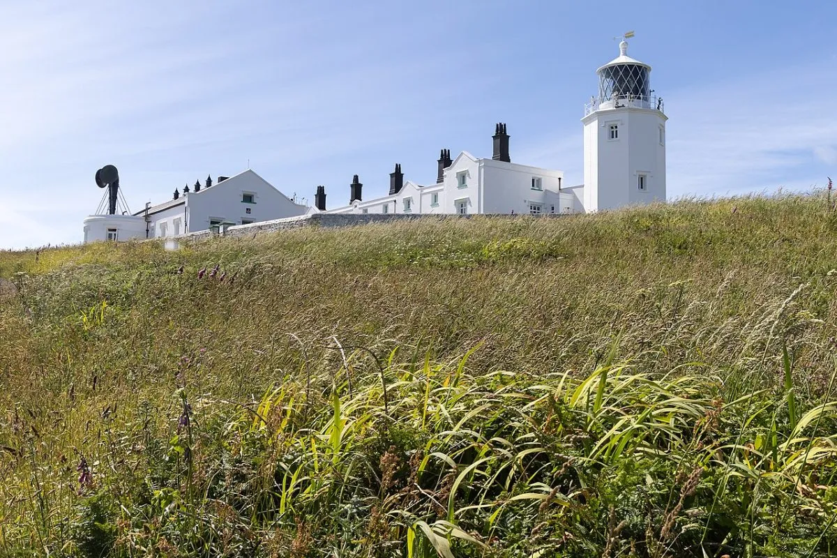 De vuurtoren van Lizard met de witte gebouwen eromheen, van een afstand zodat de ligging op de kop van het schiereiland te zien is.