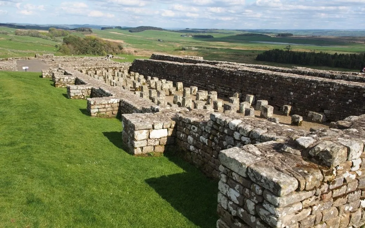 De resten van Housesteads Roman Fort op de helling, met de fundamenten van de gebouwen en het landschap erachter.