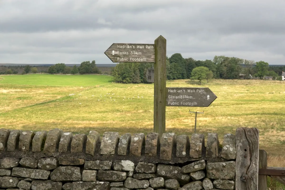 Een bord of paal van de Hadrian's Wall Path met het eikeltje van de National Trails, met het pad naast de muur erachter.