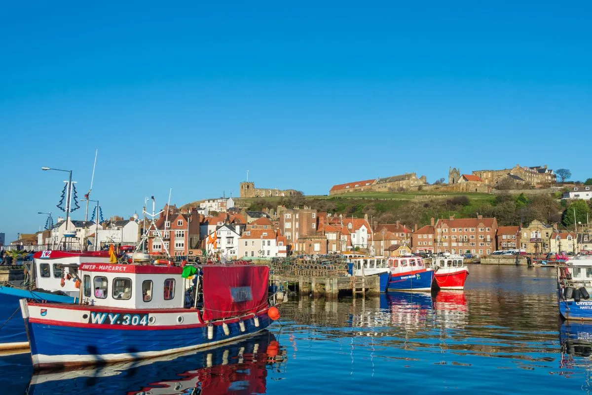 De haven van Whitby met de vissersboten en de ruïne van de abdij op de klif erboven.
